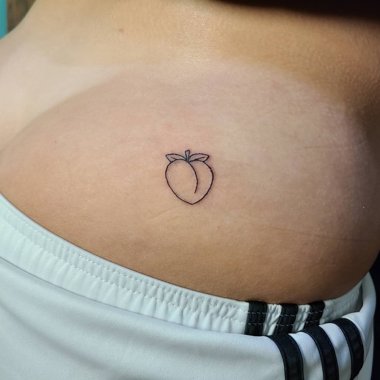 Outline of a peach tattoo on the side of the torso